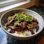 A close-up of a Korean Beef Bowl (Bulgogi) served over white rice, topped with fresh green onions and sesame seeds.