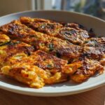 A close-up of golden-brown Korean Kimchi Pancakes (Pajeon) arranged on a white plate, showcasing their crispy edges and green scallions.