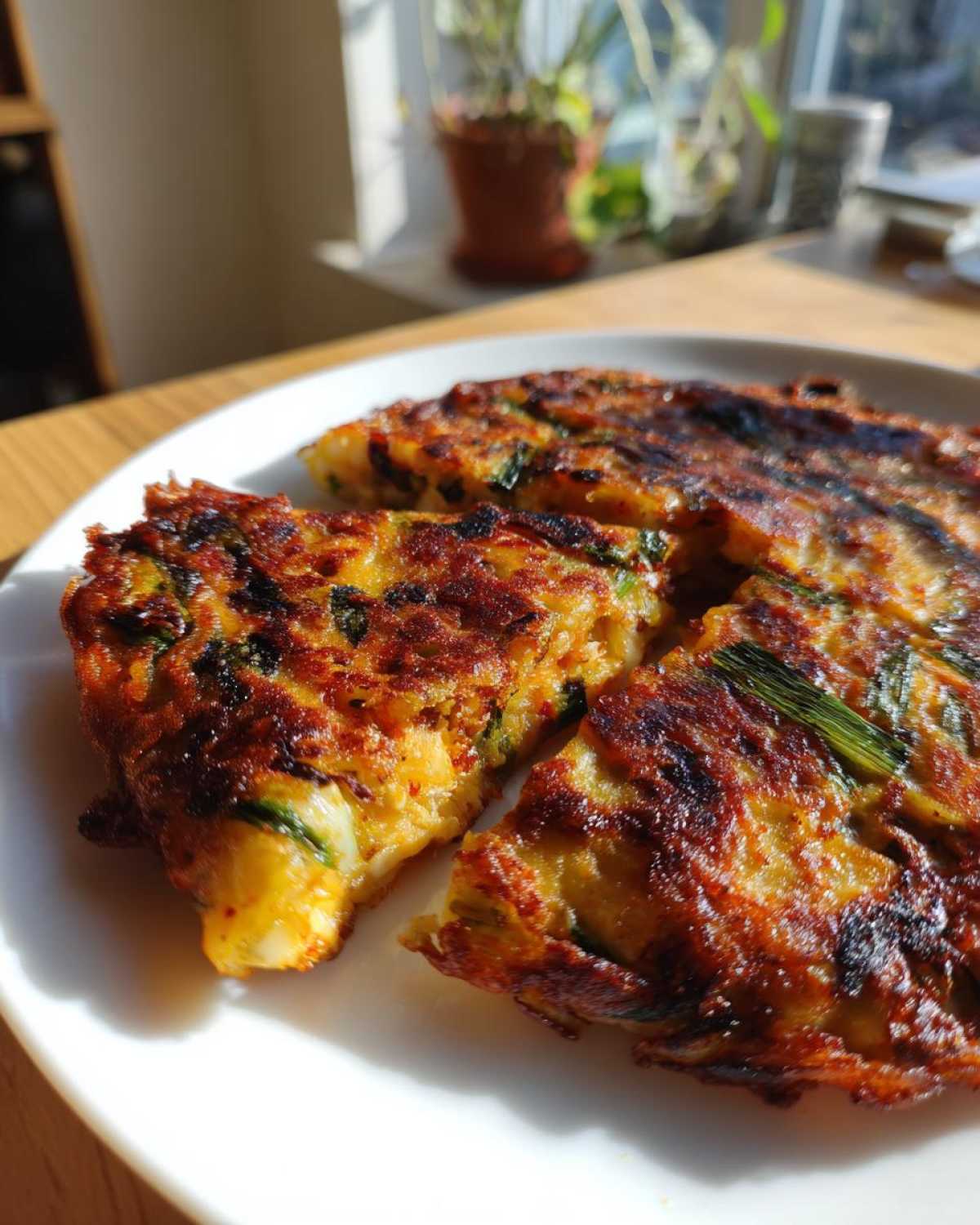 A close-up of crispy Korean Kimchi Pancakes (Pajeon) on a white plate, showcasing the golden-brown texture and green scallions.