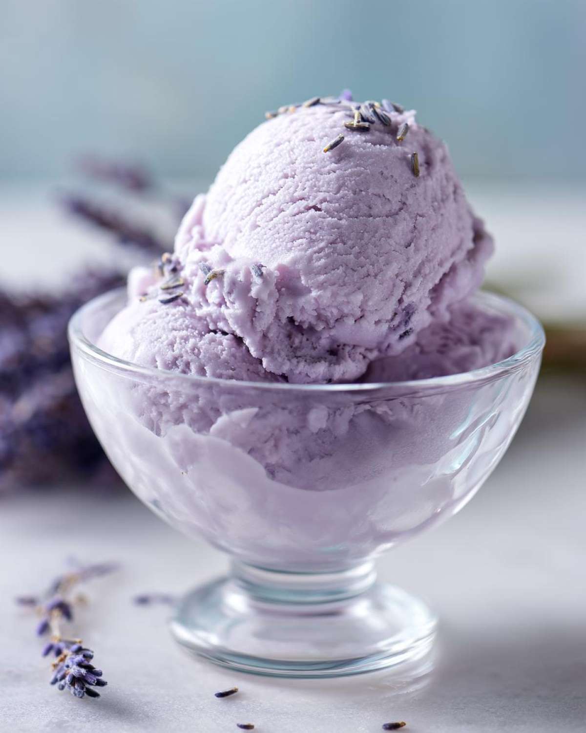 Two scoops of creamy lavender honey ice cream in a glass bowl, garnished with dried lavender buds.