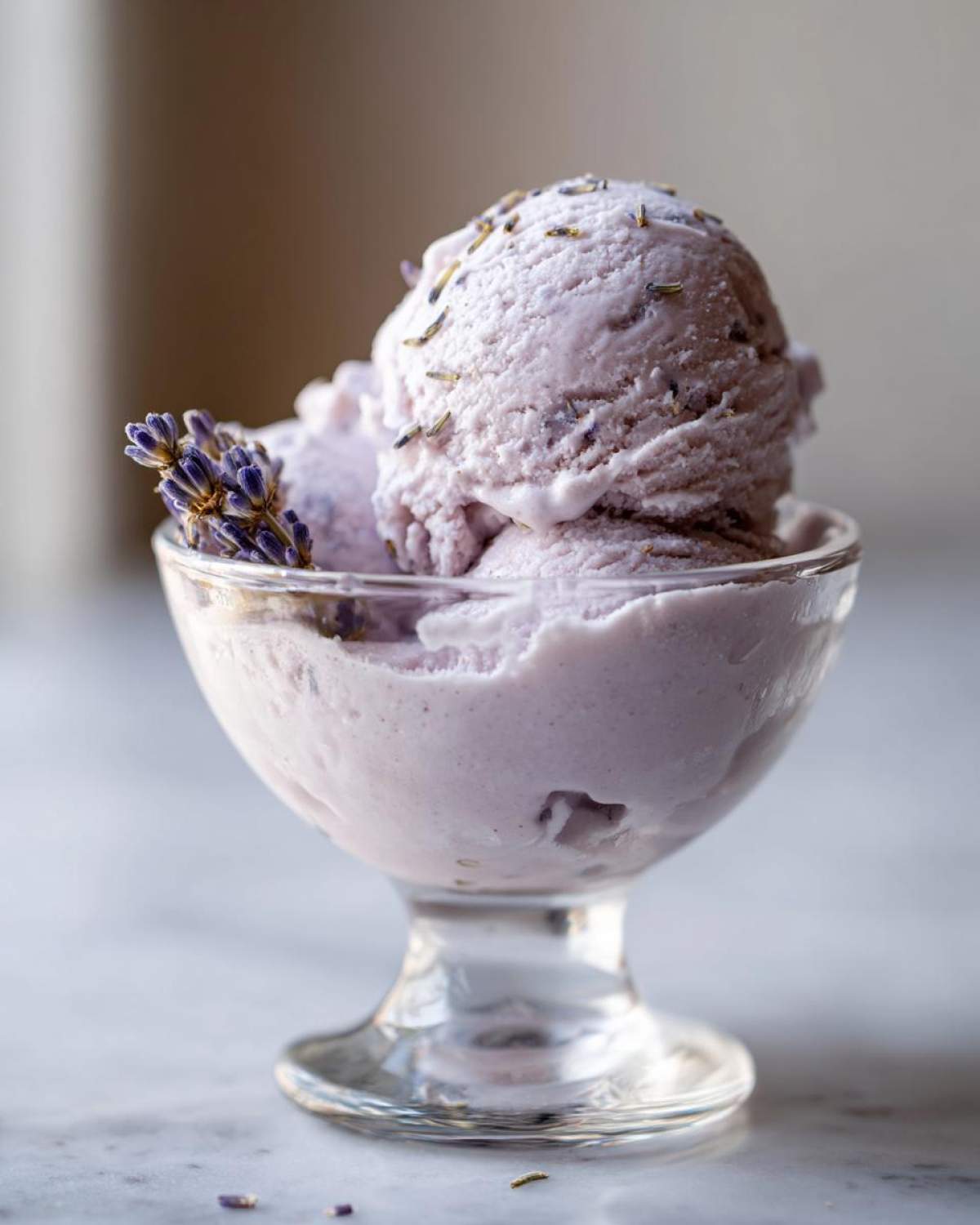 Close-up of creamy Lavender Honey Ice Cream in a glass bowl, garnished with lavender sprigs.