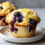 A close-up of a delicious lemon blueberry muffin topped with blueberries and lemon zest.