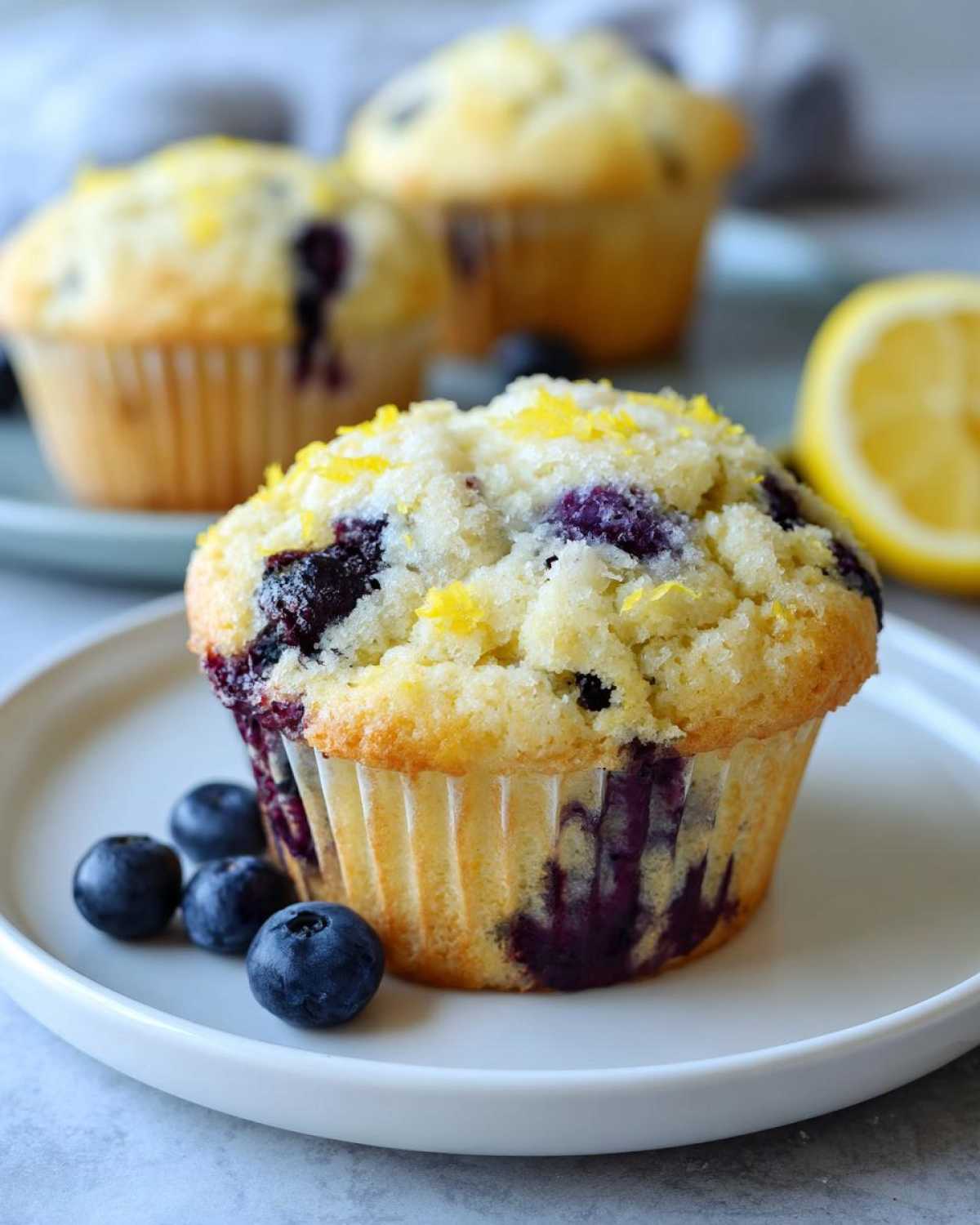 Close-up of a perfect lemon blueberry muffin topped with lemon zest and sugar, with fresh blueberries on the side.