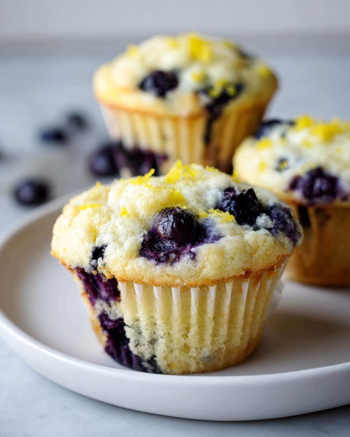 Close-up of three perfect lemon blueberry muffins topped with fresh blueberries and lemon zest.