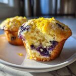 Close-up of a perfect lemon blueberry muffin, split open to reveal blueberries and topped with lemon zest.