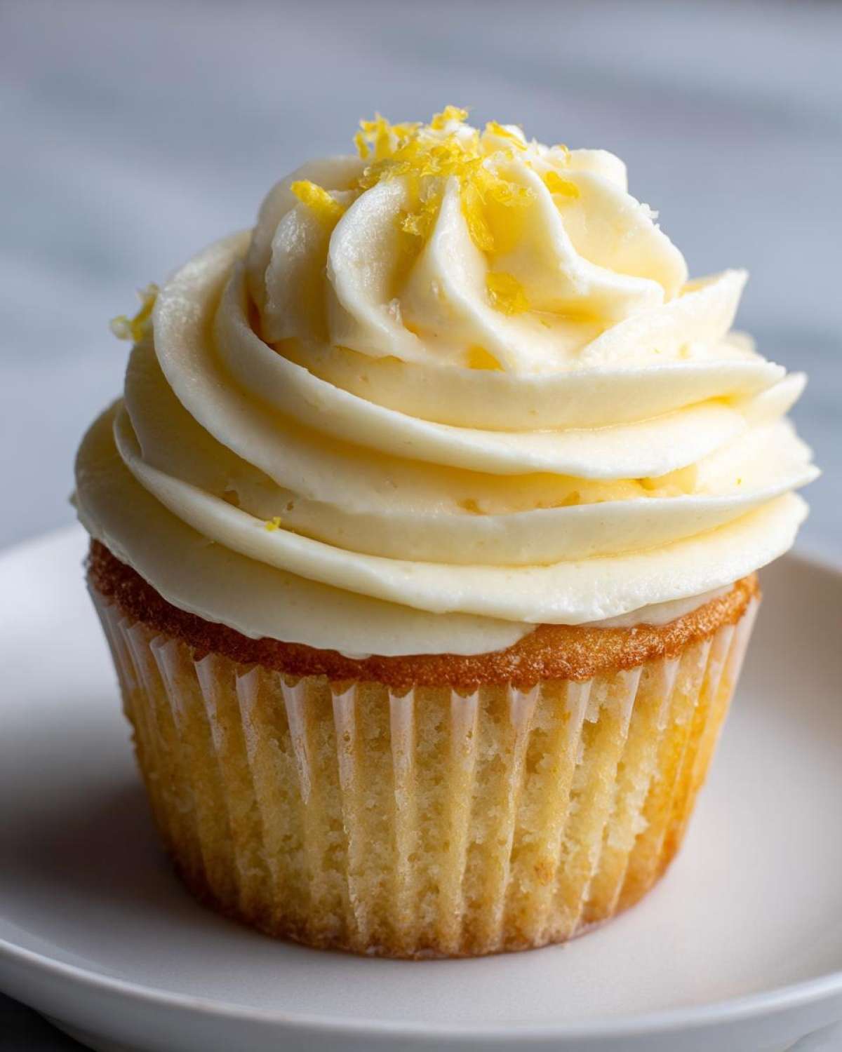 A close-up of a perfectly baked Lemon Vanilla Cupcake topped with creamy frosting and lemon zest.