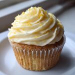 A close-up of a delicious Lemon Vanilla Cupcake with fluffy, swirled frosting and a sprinkle of lemon zest.