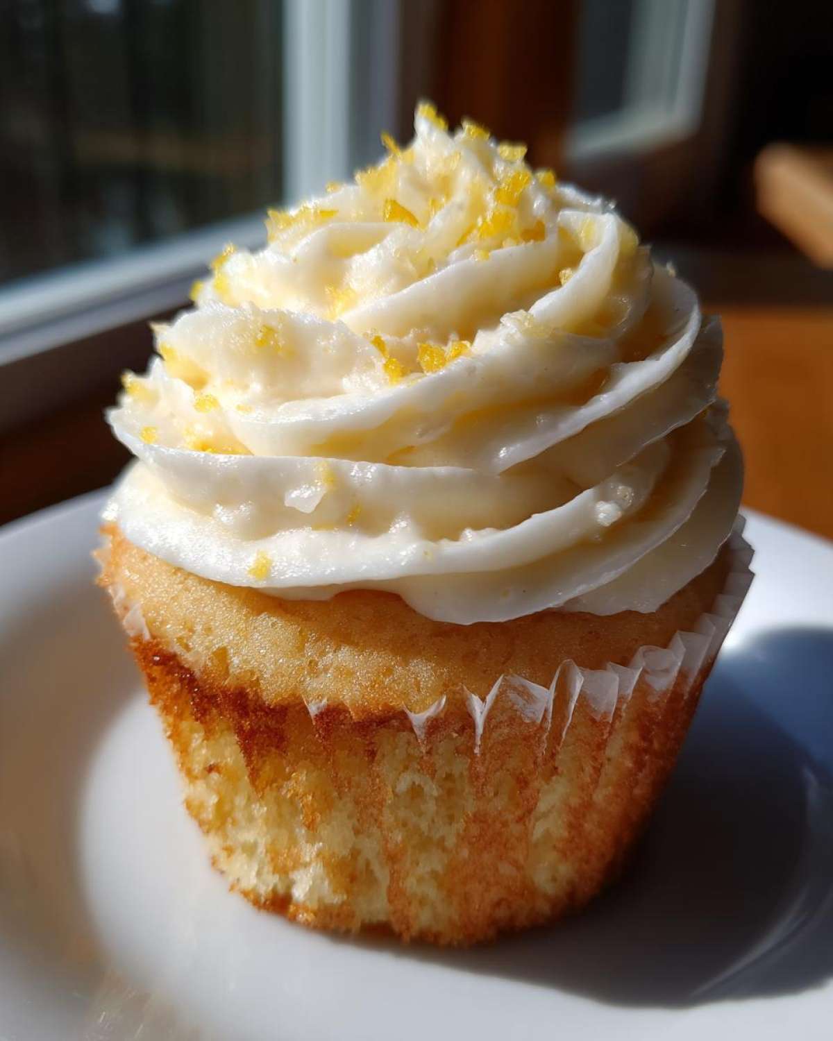 A close-up of a fluffy Lemon Vanilla Cupcake topped with creamy white frosting and sprinkled with lemon zest.