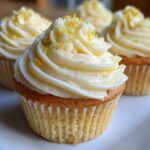 Close-up of a plate with four Lemon Vanilla Cupcakes, topped with creamy white frosting and lemon zest.