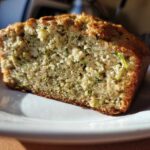 A close-up view of a moist slice of Lemon Zucchini Bread on a white plate.