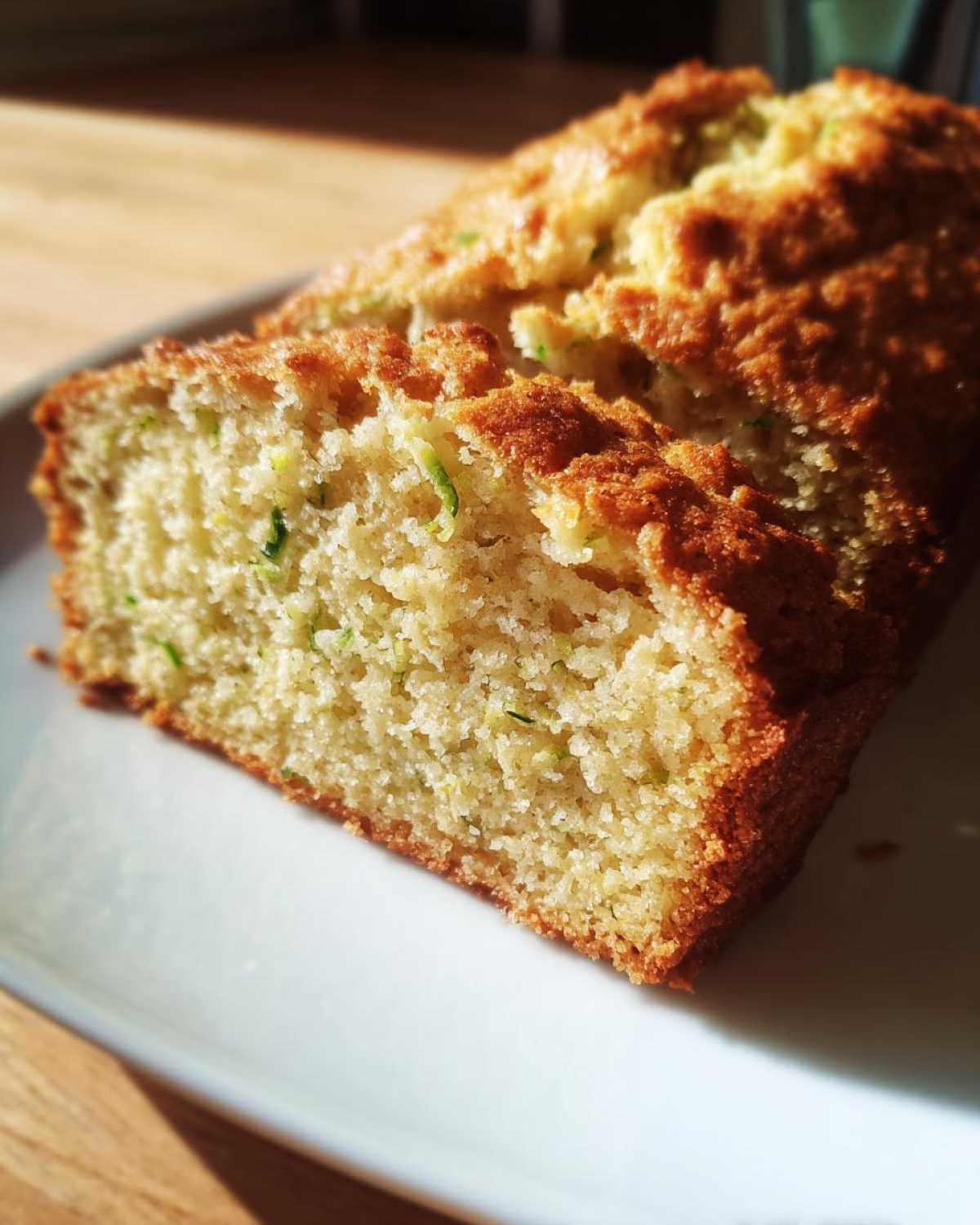 A close-up of a slice of moist Lemon Zucchini Bread on a white plate, showing the tender crumb and flecks of zucchini.
