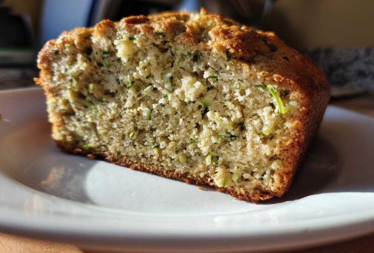 A close-up view of a moist slice of Lemon Zucchini Bread on a white plate.