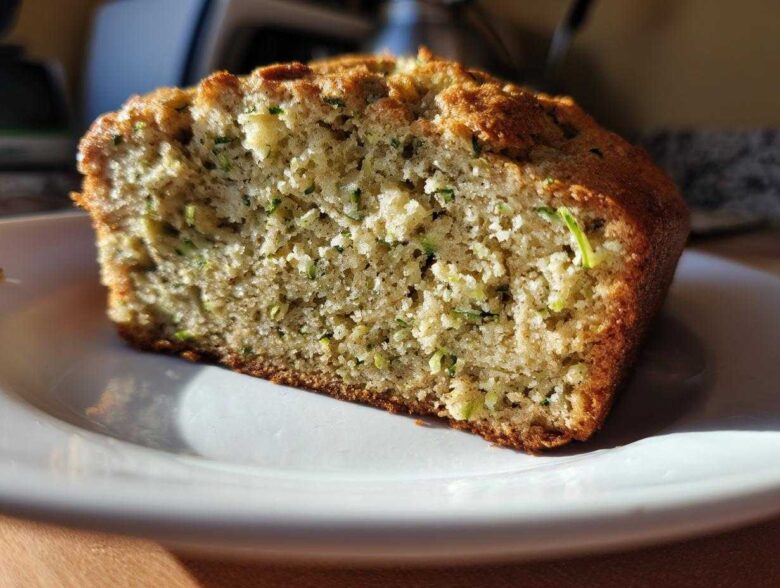 A close-up view of a moist slice of Lemon Zucchini Bread on a white plate.