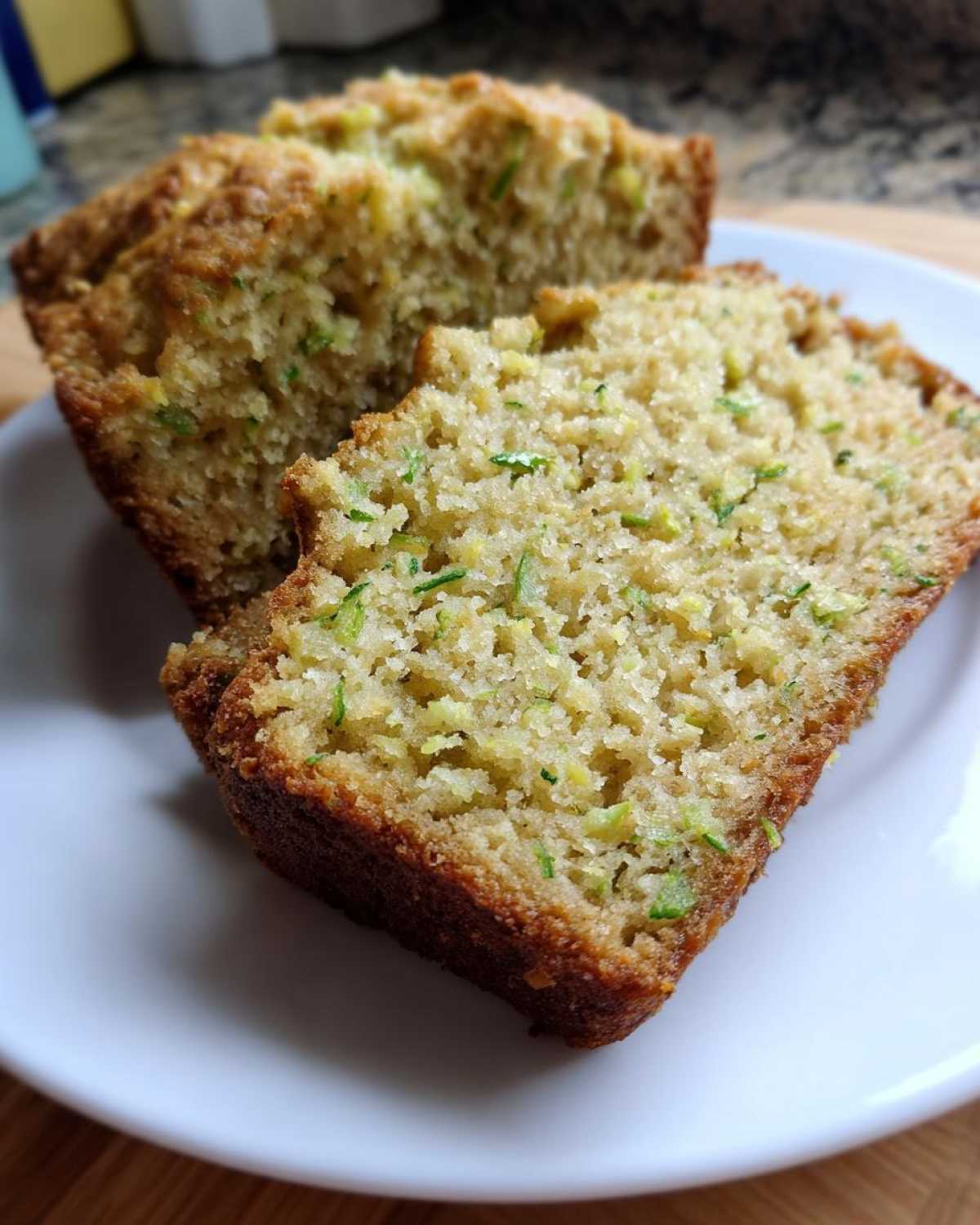 Close-up of two slices of moist Lemon Zucchini Bread on a white plate, showcasing the tender crumb and flecks of zucchini.