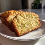 Close-up of two moist slices of Lemon Zucchini Bread on a white plate, showing the texture and green flecks of zucchini.