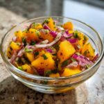 A close-up of a glass bowl filled with vibrant Mango Mango Salad, featuring diced ripe mangoes, red onion, and fresh cilantro.