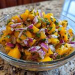 Close-up of a glass bowl filled with a vibrant Mango Mango Salad, featuring diced ripe mangoes, red onion, and fresh cilantro.