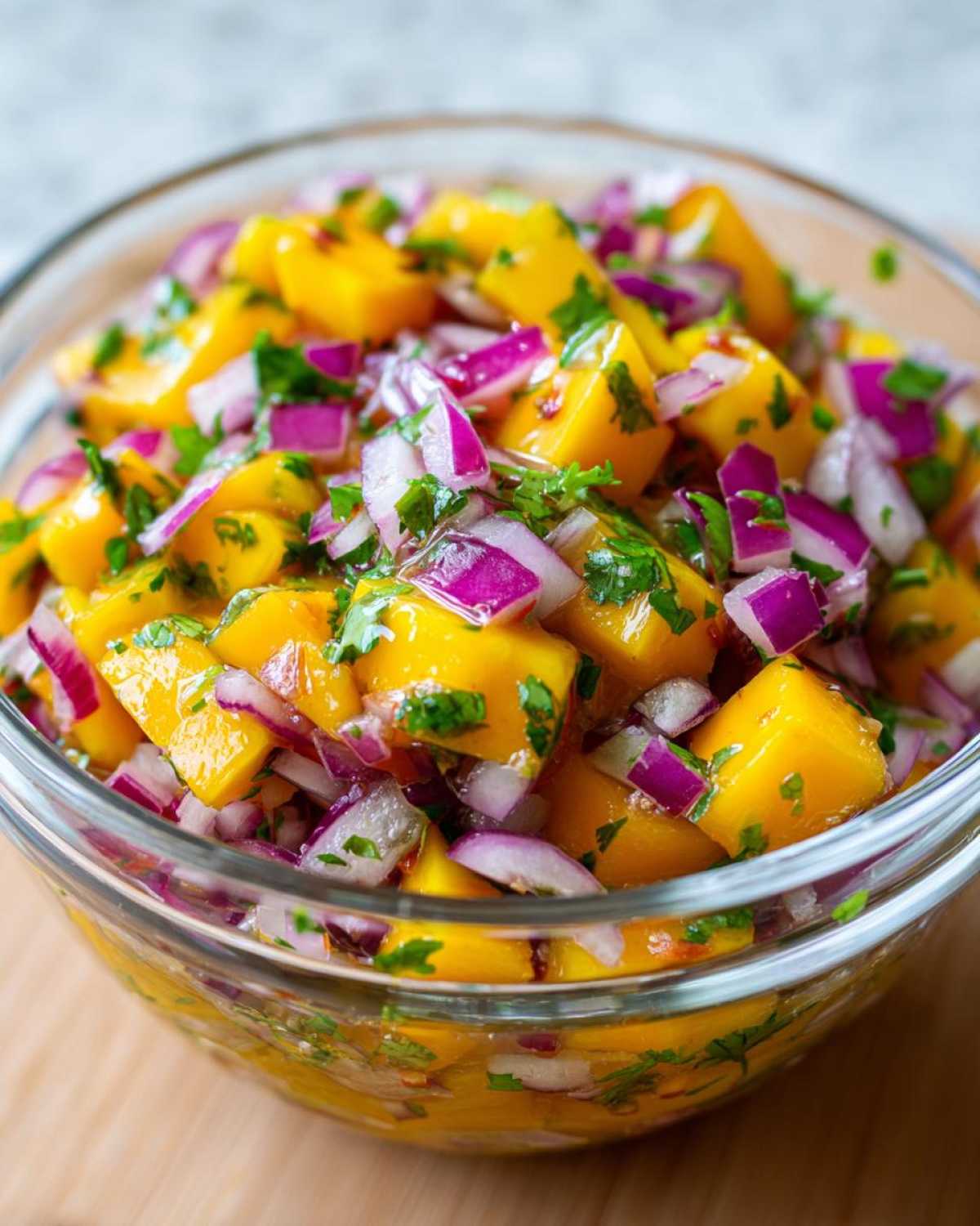 A close-up of a glass bowl filled with a vibrant Mango Mango Salad, featuring diced ripe mangoes, red onion, and fresh cilantro.