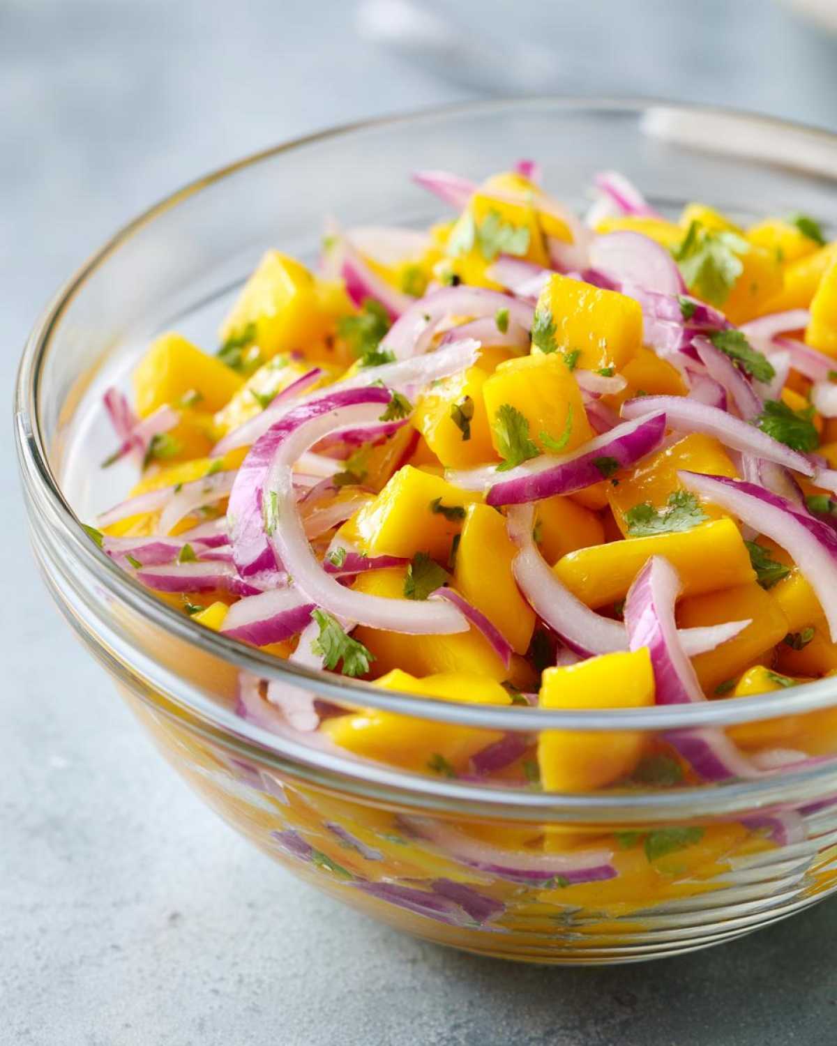 Close-up of a vibrant Mango Mango Salad in a glass bowl, featuring diced ripe mangoes, thinly sliced red onions, and fresh cilantro.
