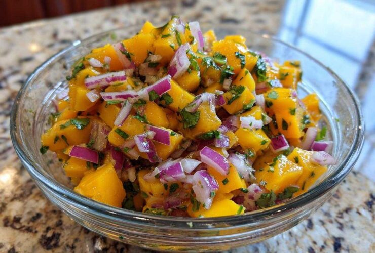 Close-up of a glass bowl filled with a vibrant Mango Mango Salad, featuring diced ripe mangoes, red onion, and fresh cilantro.