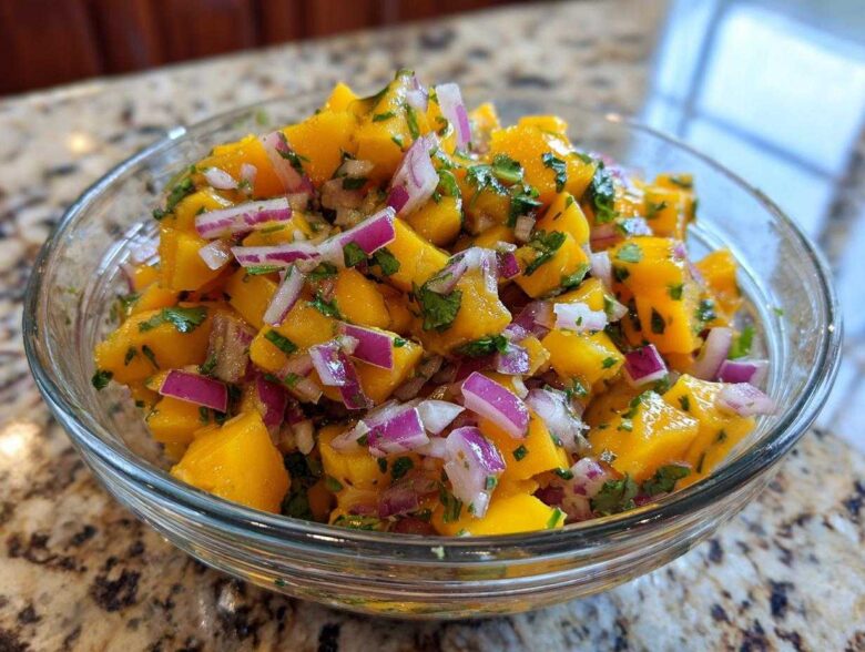 Close-up of a glass bowl filled with a vibrant Mango Mango Salad, featuring diced ripe mangoes, red onion, and fresh cilantro.
