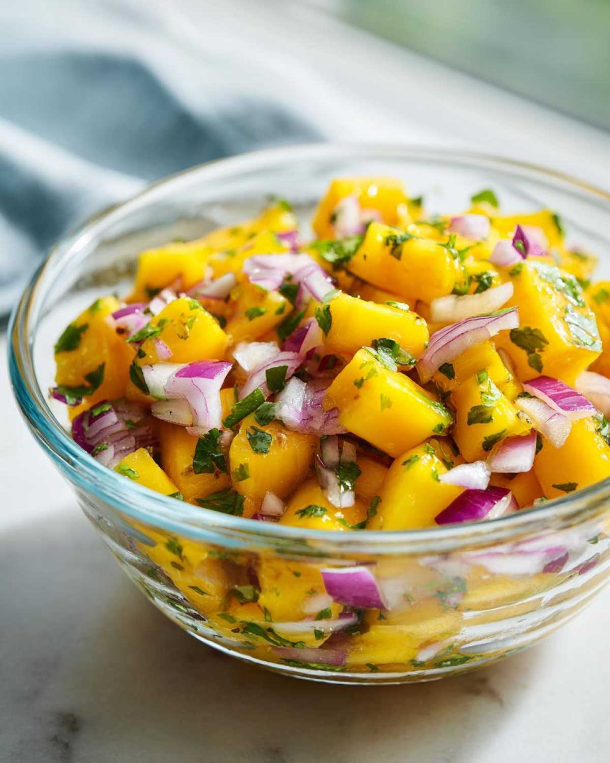 A close-up of a glass bowl filled with vibrant Mango Mango Salad, featuring diced ripe mangoes, red onion, and fresh cilantro.
