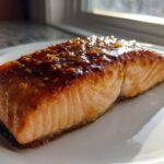 A perfectly cooked Maple Dijon Salmon fillet glistening with a sweet glaze and sprinkled with sesame seeds, served on a white plate.