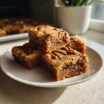 Three Maple Pecan Swirl Blondies stacked on a white plate, showcasing their gooey center and pecan topping.