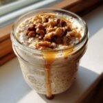 A close-up of Maple Walnut Overnight Oats in a glass jar, topped with walnuts and drizzled with syrup.
