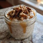 A close-up of Maple Walnut Overnight Oats served in a glass jar, topped with walnuts and drizzled with maple syrup.