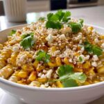 A close-up of a vibrant Mexican street corn bowl topped with crumbled cheese, chili powder, and fresh cilantro.