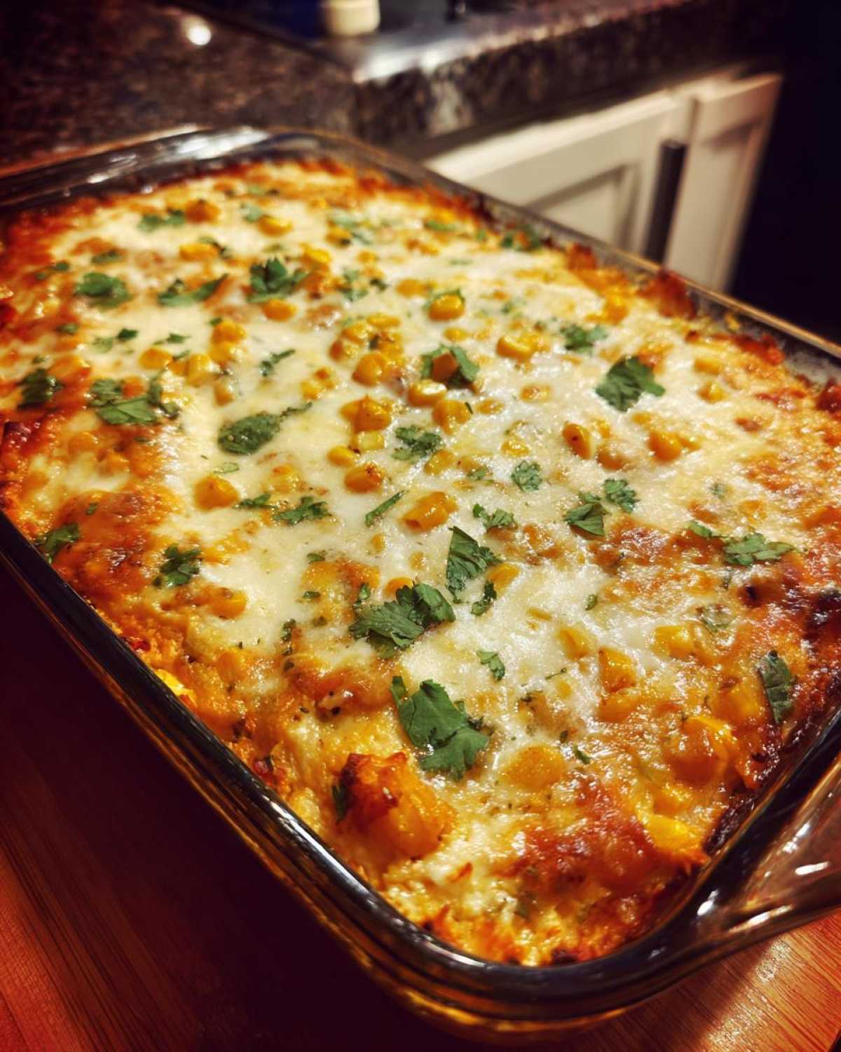 A close-up of bubbling Mexican street corn dip, topped with melted cheese, corn kernels, and fresh cilantro, served in a glass baking dish.