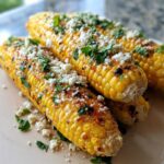 Close-up of grilled Mexican street corn, topped with crumbled cheese, chopped cilantro, and chili powder.