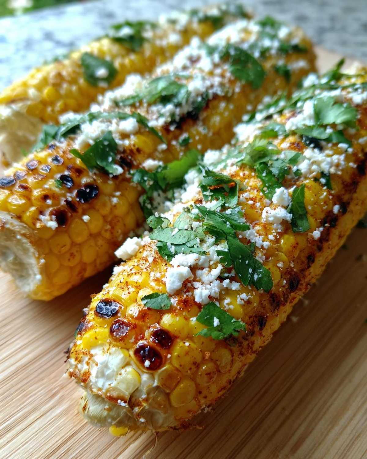 Close-up of grilled Mexican street corn topped with crumbled cheese, chopped cilantro, and chili powder.