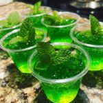 Close-up of several green Mint Julep Jello Shots garnished with fresh mint leaves.