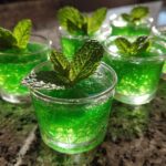 Close-up of several vibrant green Mint Julep Jello Shots, each garnished with a fresh mint leaf.