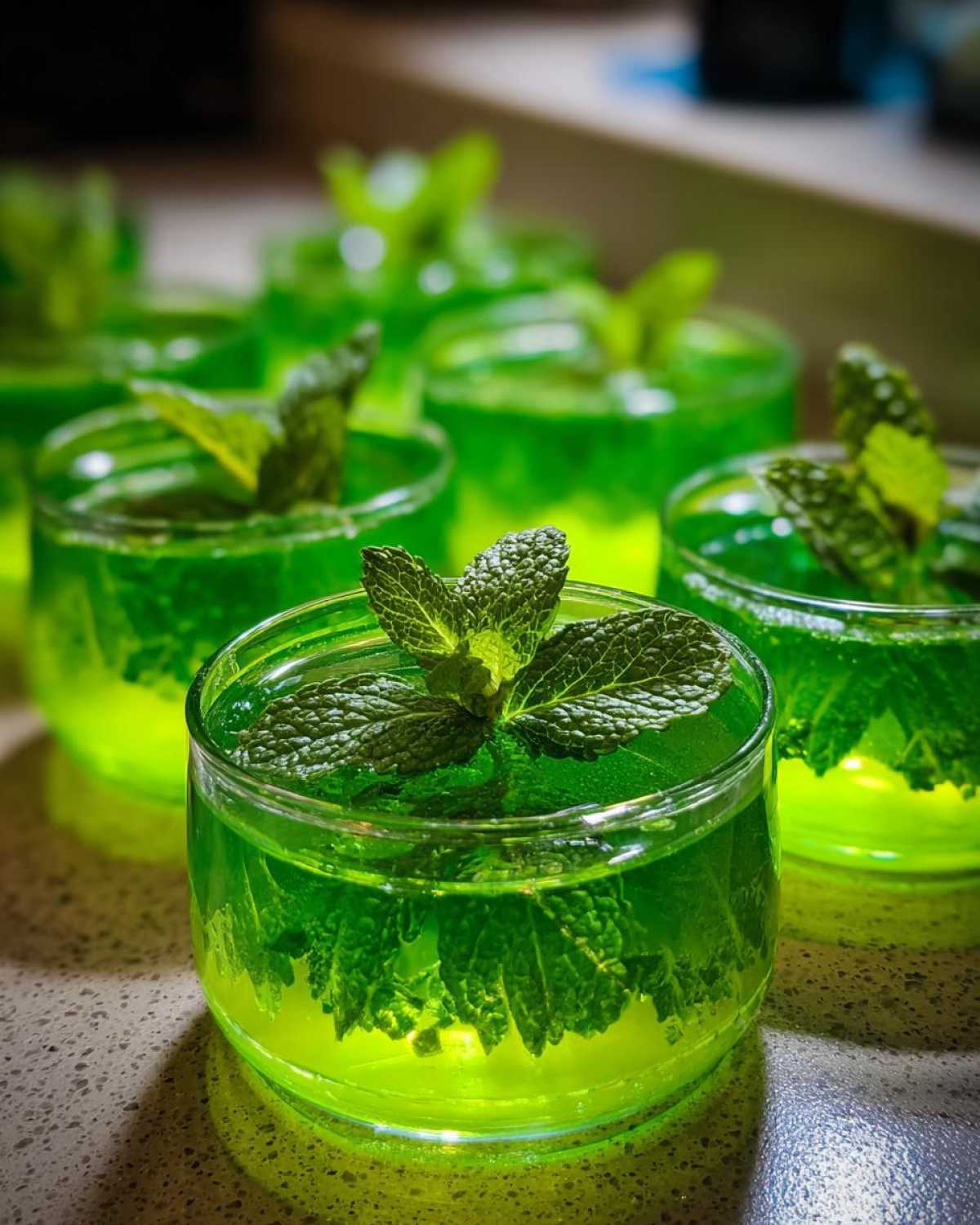 Close-up of several Mint Julep Jello Shots, each garnished with fresh mint leaves, in clear glasses.