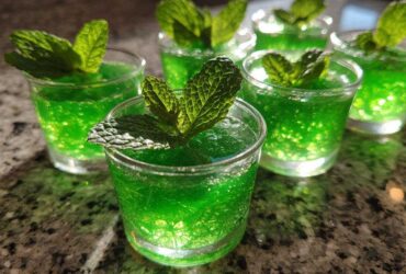 Close-up of several vibrant green Mint Julep Jello Shots, each garnished with a fresh mint leaf.