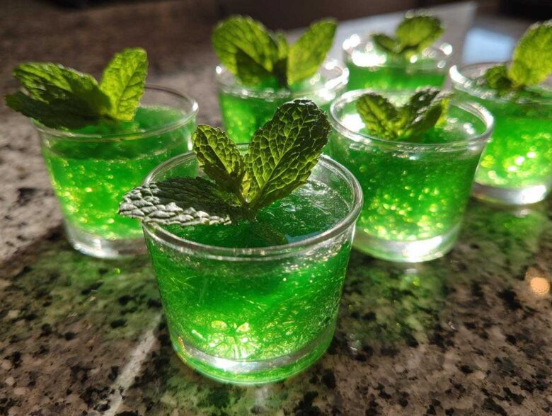Close-up of several vibrant green Mint Julep Jello Shots, each garnished with a fresh mint leaf.