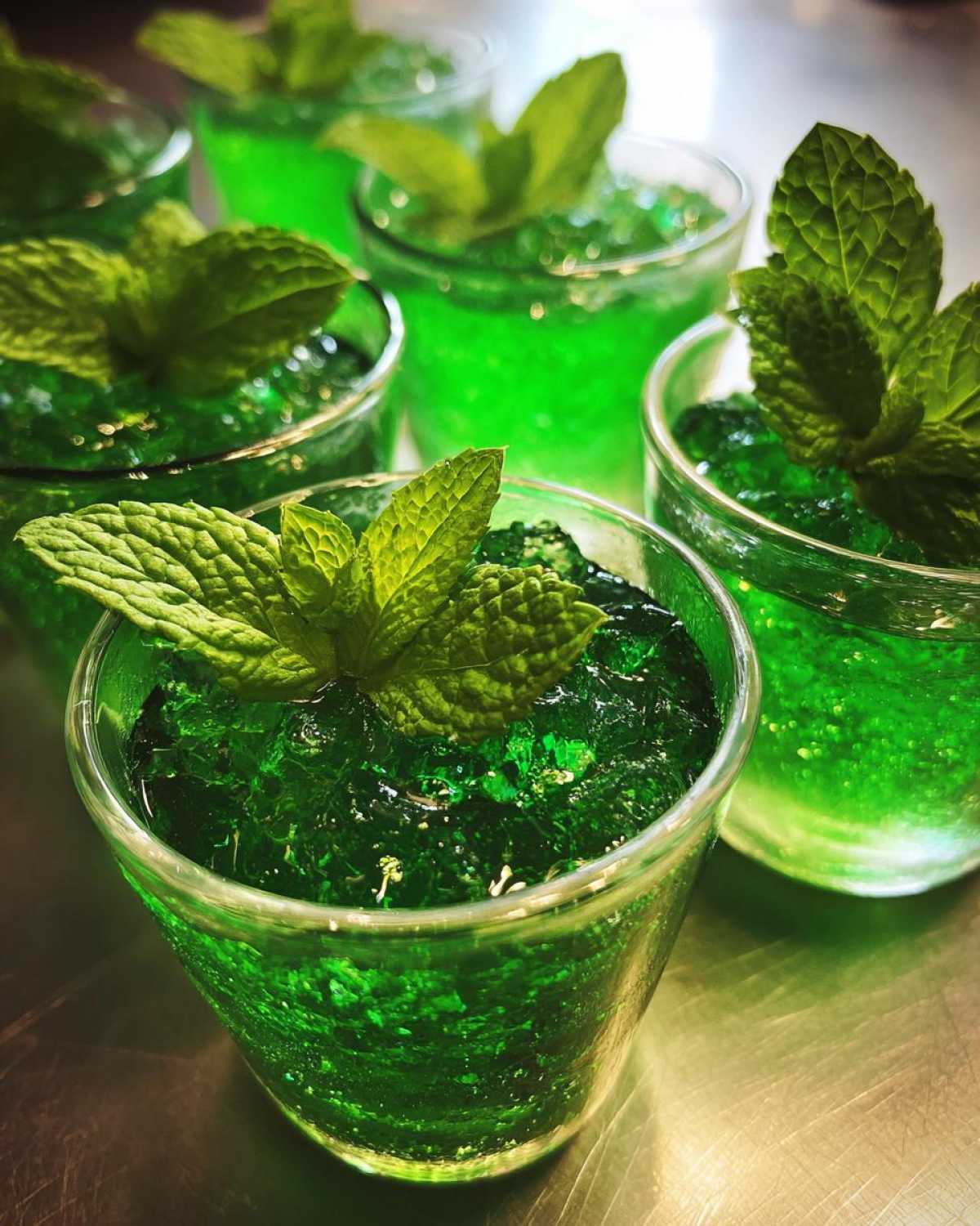Close-up of several vibrant green Mint Julep Jello Shots, each topped with a fresh mint leaf.