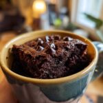 A close-up of a delicious Mocha Mug Brownie topped with chocolate chips, held in a mug.