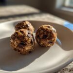 Three homemade Oatmeal Chocolate Chip Energy Bites arranged on a white plate, bathed in natural light.