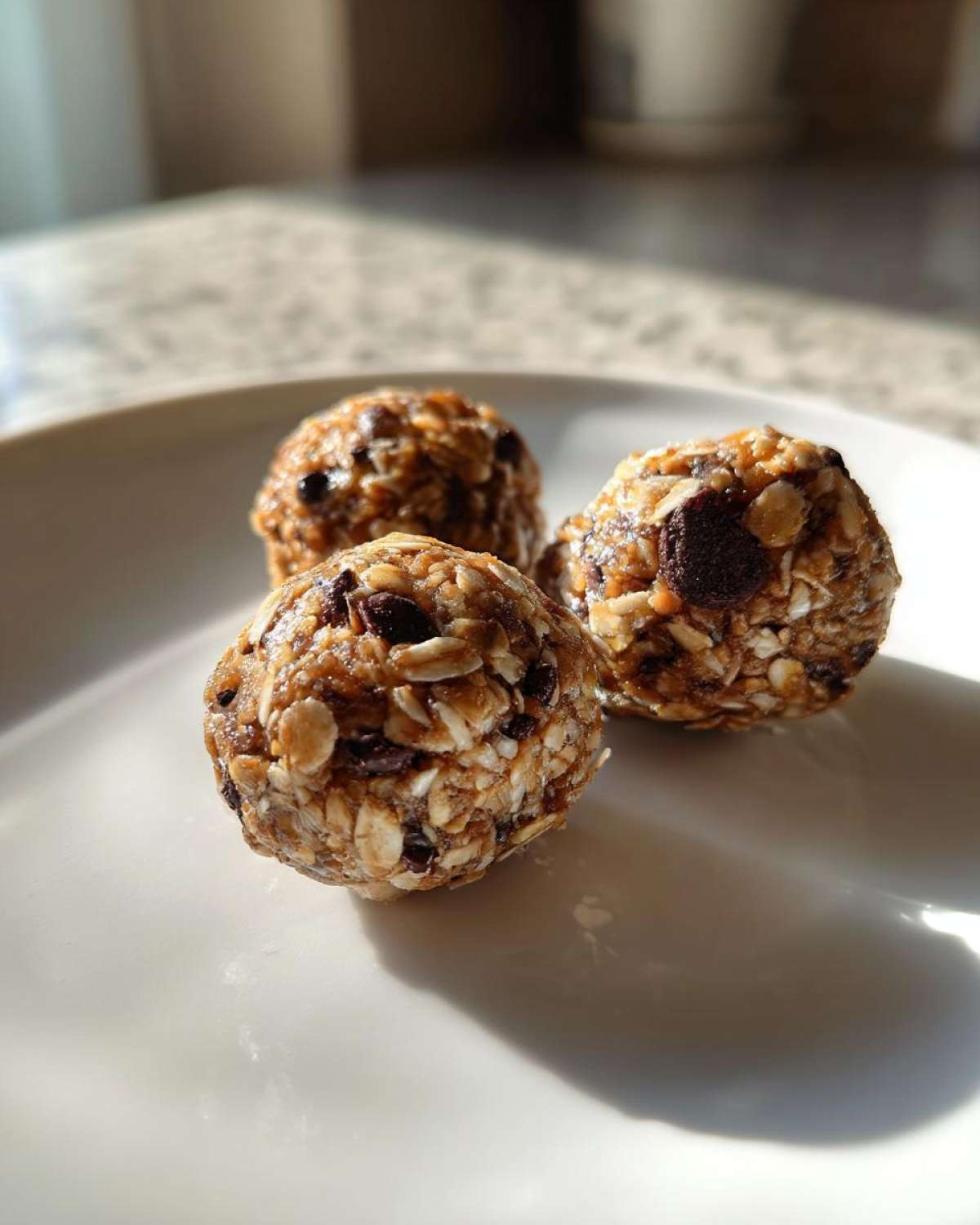 Three Oatmeal Chocolate Chip Energy Bites on a white plate, close-up shot.