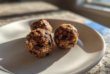 Three homemade Oatmeal Chocolate Chip Energy Bites arranged on a white plate, bathed in natural light.