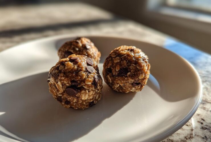 Three homemade Oatmeal Chocolate Chip Energy Bites arranged on a white plate, bathed in natural light.