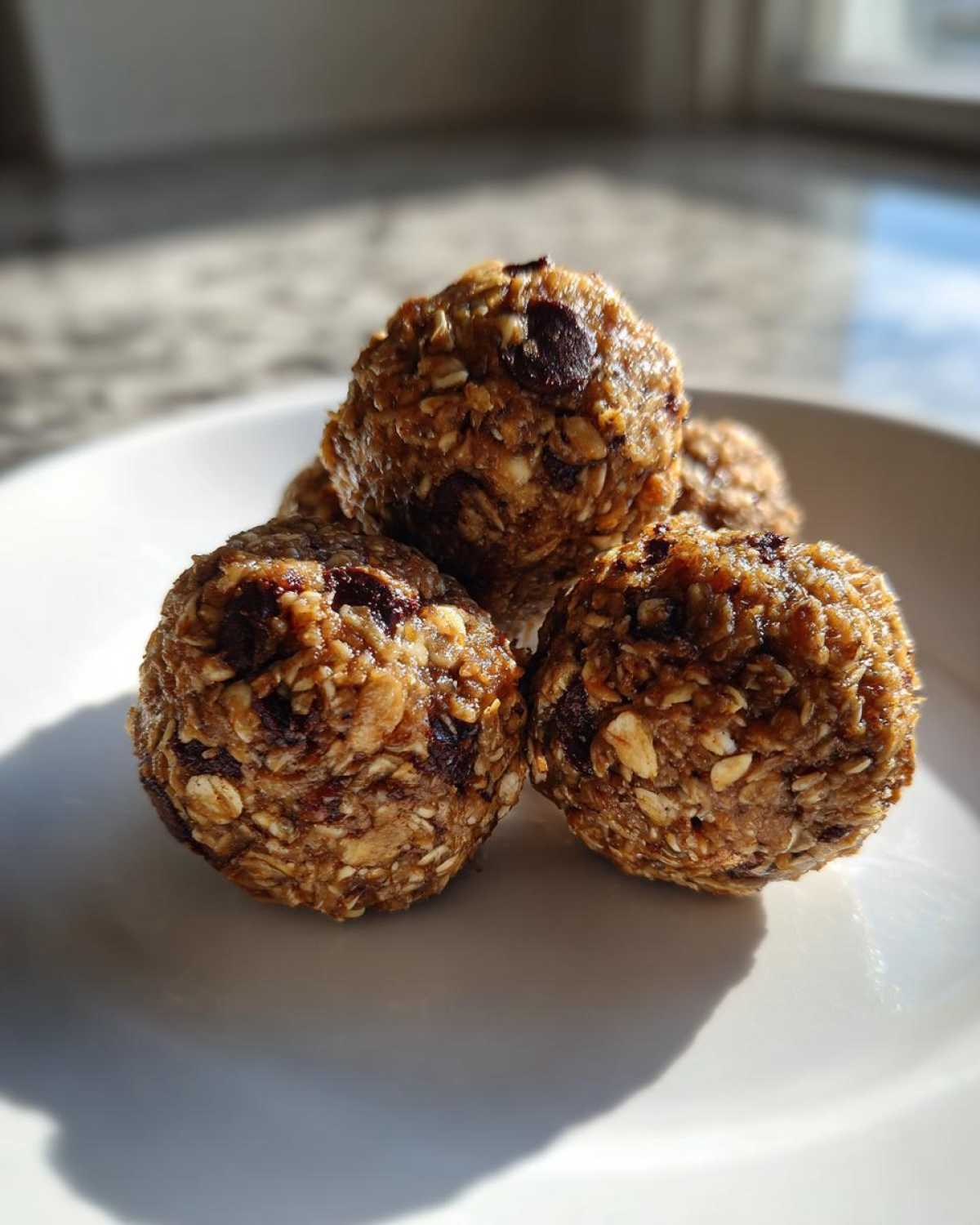 Close-up of several Oatmeal Chocolate Chip Energy Bites stacked on a white plate, showcasing oats and chocolate chips.