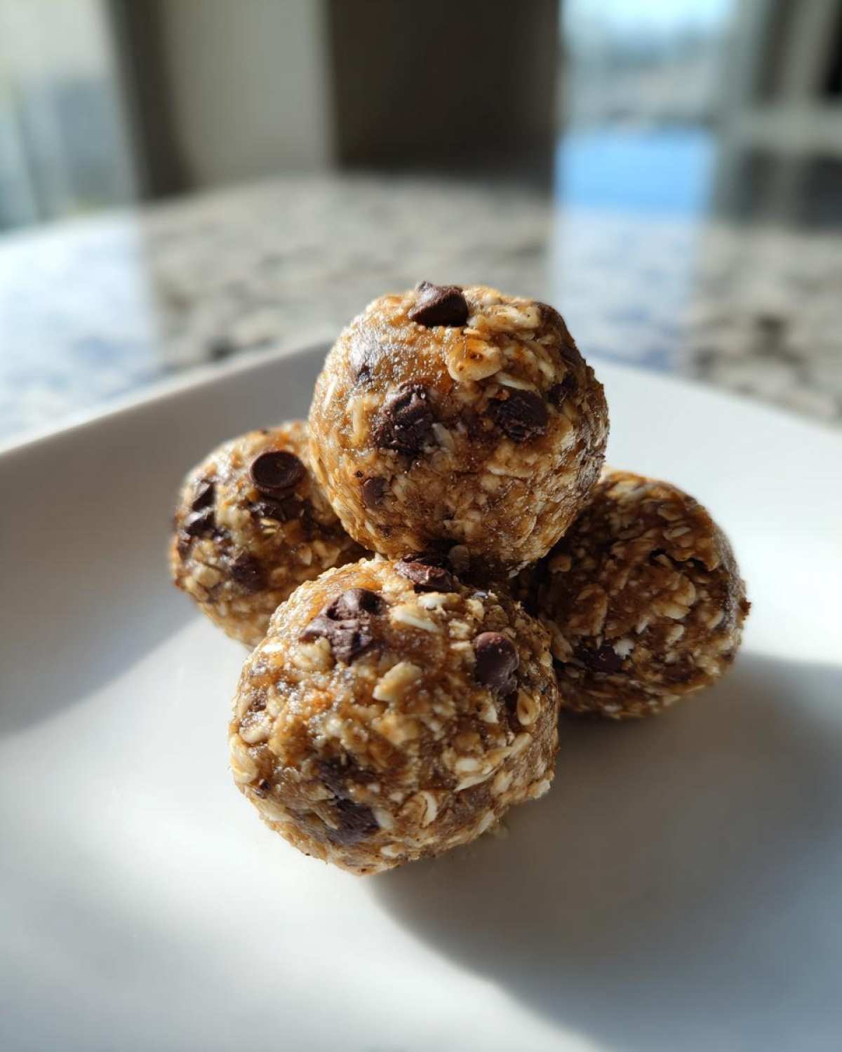 A close-up of a stack of four Oatmeal Chocolate Chip Energy Bites on a white plate.