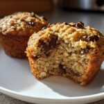 Close-up of two delicious Oatmeal Chocolate Chip Muffins on a white plate, one with a bite taken out, revealing the texture.