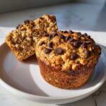 Close-up of two delicious oatmeal chocolate chip muffins on a white plate, one cut in half to show the texture.
