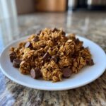 A pile of delicious Peanut Butter Cup Granola with chunks of chocolate on a white plate.